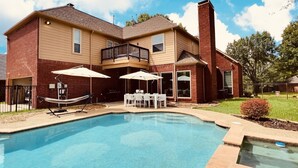 A two-story house with a swimming pool, outdoor furniture, and a barbecue grill.