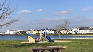 A park with a playground, a picnic table, and a lake in the background. - Exceptional seafront location (Étel)