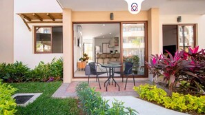 Un patio moderno al aire libre con zona de comedor, rodeado de exuberante vegetación y un jardín cuidado.