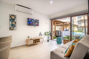 A living room with a television, a sofa, a coffee table, and a view of an outdoor pool area. - Stylish condo in Mazatlan l Pool & Terrace (Mazatlán)