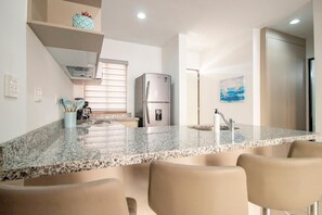 A kitchen with granite countertops, a refrigerator, a sink, and a dining area with chairs.