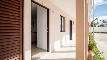 A building entrance with a closed wooden door, a visible interior hallway, and a clear sky.