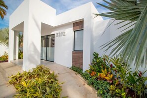 Ein modernes Gebäude mit weißer Fassade, einer gut sichtbaren Hausnummer und einem gepflegten Gartenbereich mit verschiedenen Pflanzen.