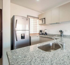 A kitchen with a stainless steel refrigerator, a built-in coffee maker, a blender, and granite countertops.