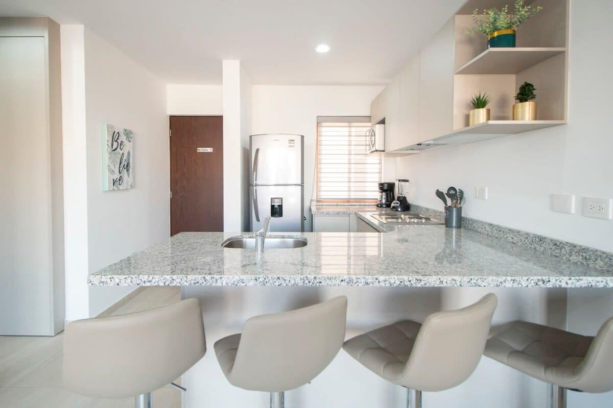 A modern kitchen with a granite countertop, stainless steel appliances, and bar stools.