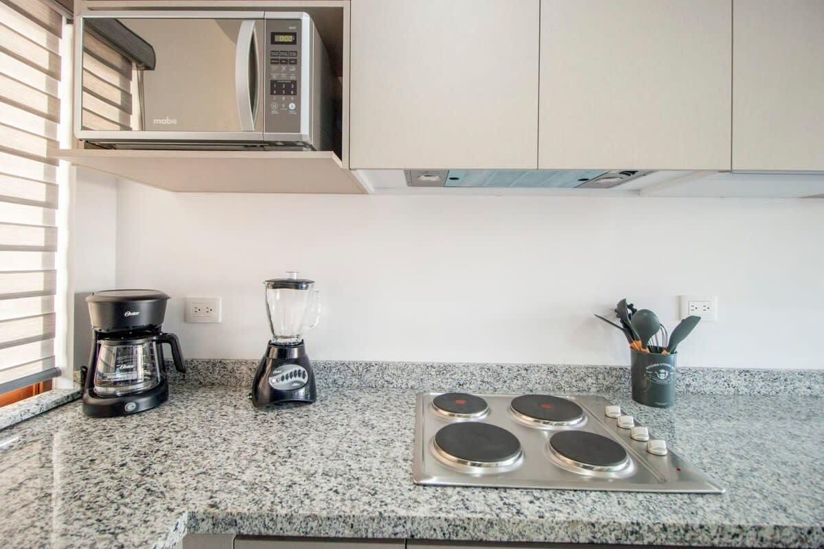 A kitchen with a microwave, coffee maker, blender, and a stove.