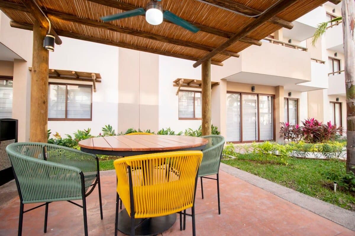 An outdoor patio with a round table and chairs, a ceiling fan, and a view of a building with large windows.
