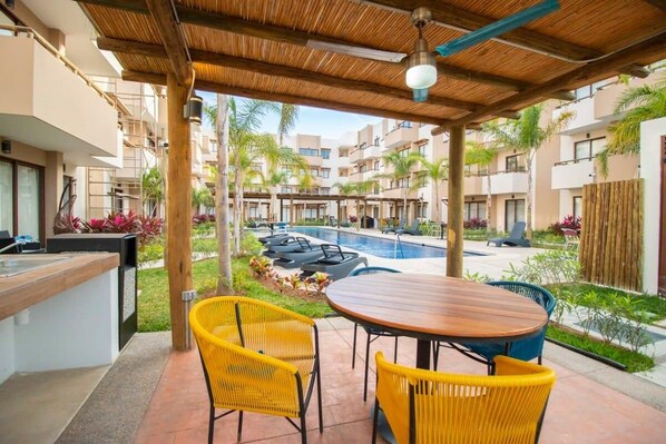 Ein überdachter Außenbereich mit einem Pool, gelben Stühlen und einem Holztisch.
