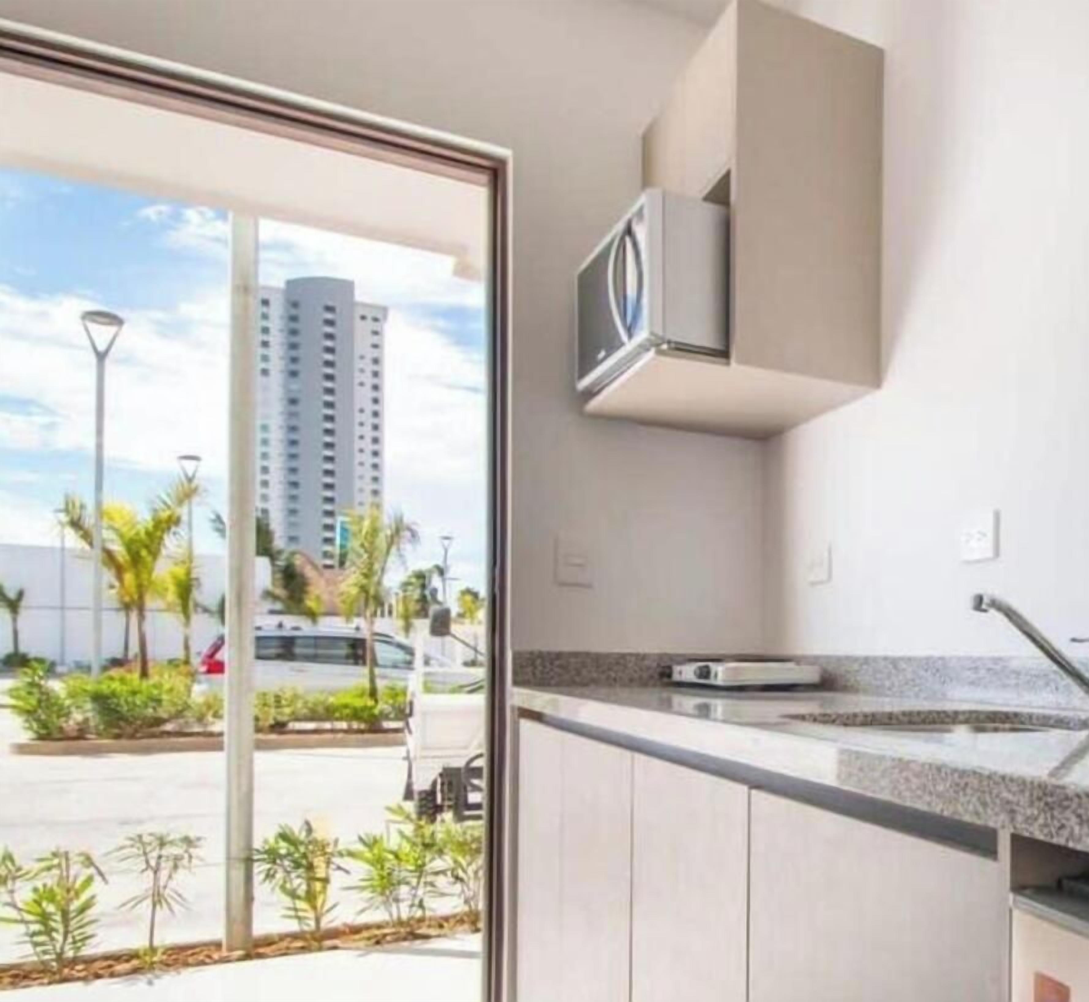 A modern kitchen with a built-in microwave, a granite countertop, and a view of a parking lot and palm trees.