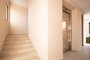 Eine Treppe führt zu einem Aufzug in einem gut beleuchteten Korridor mit Fliesenboden.