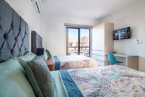 Ein Hotelzimmer mit zwei Betten, einem Schreibtisch, einem Stuhl und einem an der Wand befestigten Fernseher.