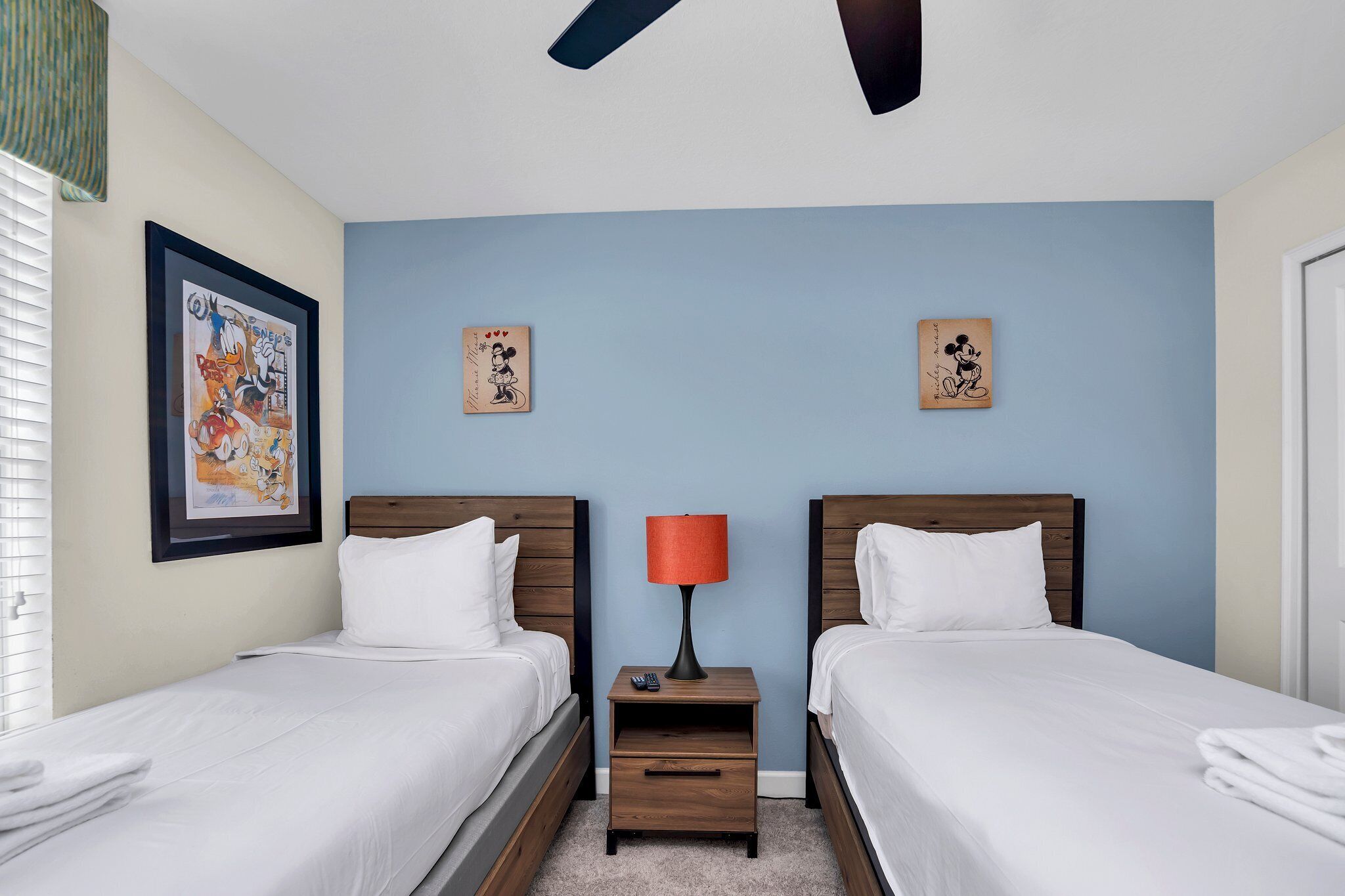 Habitación de hotel con dos camas, una mesita de noche con lámpara y obras de arte en las paredes.