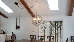 A dining area with a wooden table, chairs, and a chandelier. There are windows with a view of trees outside. - Stunning Lakehouse with all the luxuries of home (Dunsford)