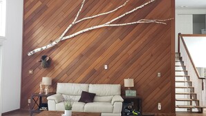 A modern living room with a herringbone wood wall, a sofa, a coffee table, and a small side table with a lamp. - Stunning Lakehouse with all the luxuries of home (Dunsford)