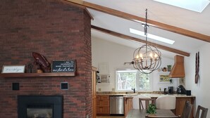 A modern kitchen with a brick fireplace, wooden dining table, and a chandelier. - Stunning Lakehouse with all the luxuries of home (Dunsford)