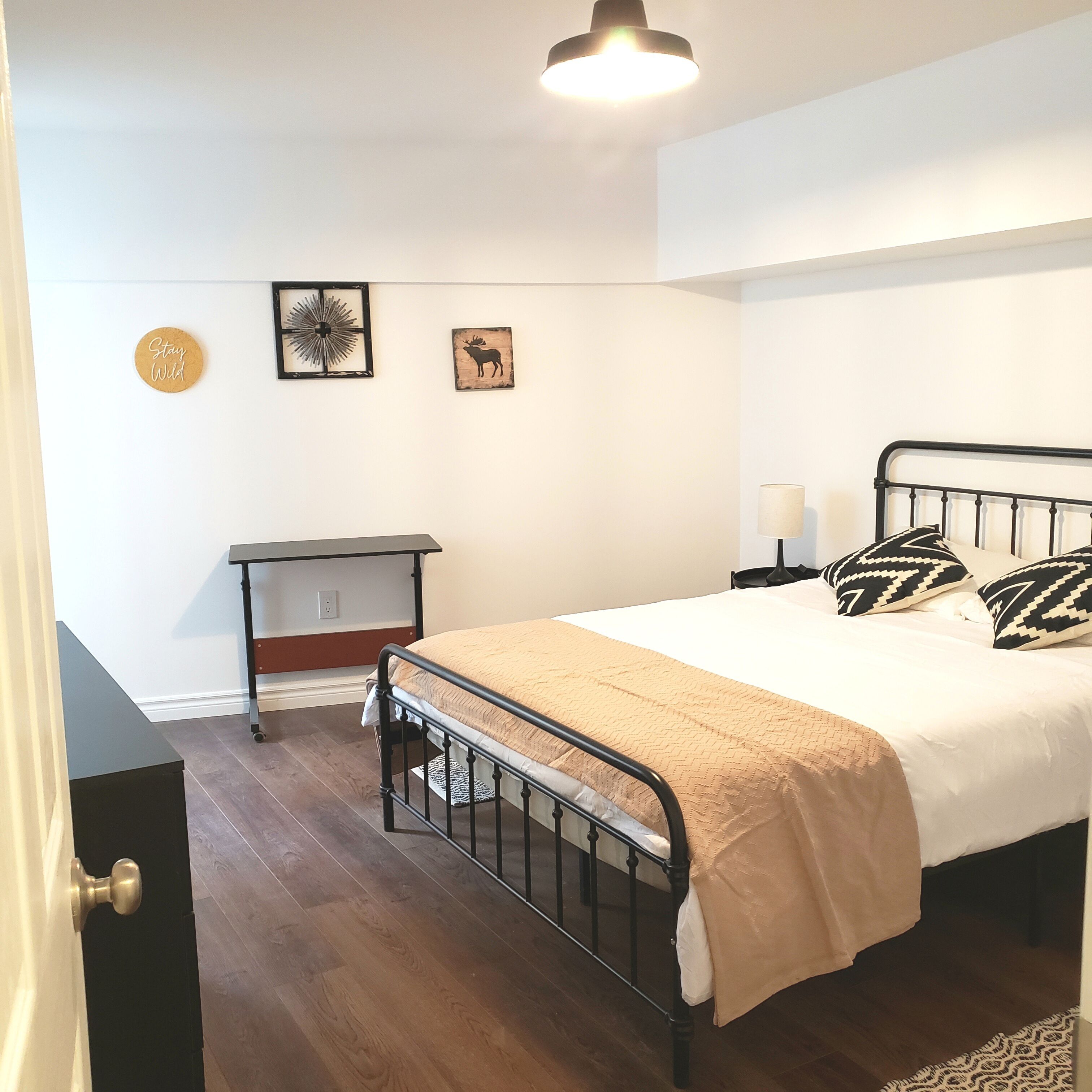 A bedroom with a bed, a nightstand, a dresser, and a wall-mounted shelf.