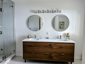 A bathroom with two round mirrors, a wooden vanity with drawers, a white sink, and a glass shower enclosure. - Stunning Lakehouse with all the luxuries of home (Dunsford)
