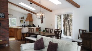 A spacious living area with a white leather sofa, wooden dining table, and a kitchen in the background. - Stunning Lakehouse with all the luxuries of home (Dunsford)