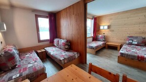 Una habitación pequeña y acogedora con paredes y suelos de madera, que cuenta con dos camas individuales con ropa de cama estampada, una mesa de madera y un banco.