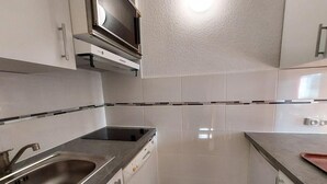 Una cocina compacta con un lavamanos de acero inoxidable, un horno empotrado y un microondas sobre la encimera.