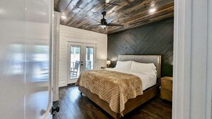 A bedroom with a wooden ceiling, a bed with a quilted blanket, a nightstand, and a ceiling fan.