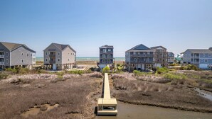 Una zona residenziale sul lungomare, con diverse case a due piani, una passerella in legno che conduce alla spiaggia e una vista aperta sull'oceano.