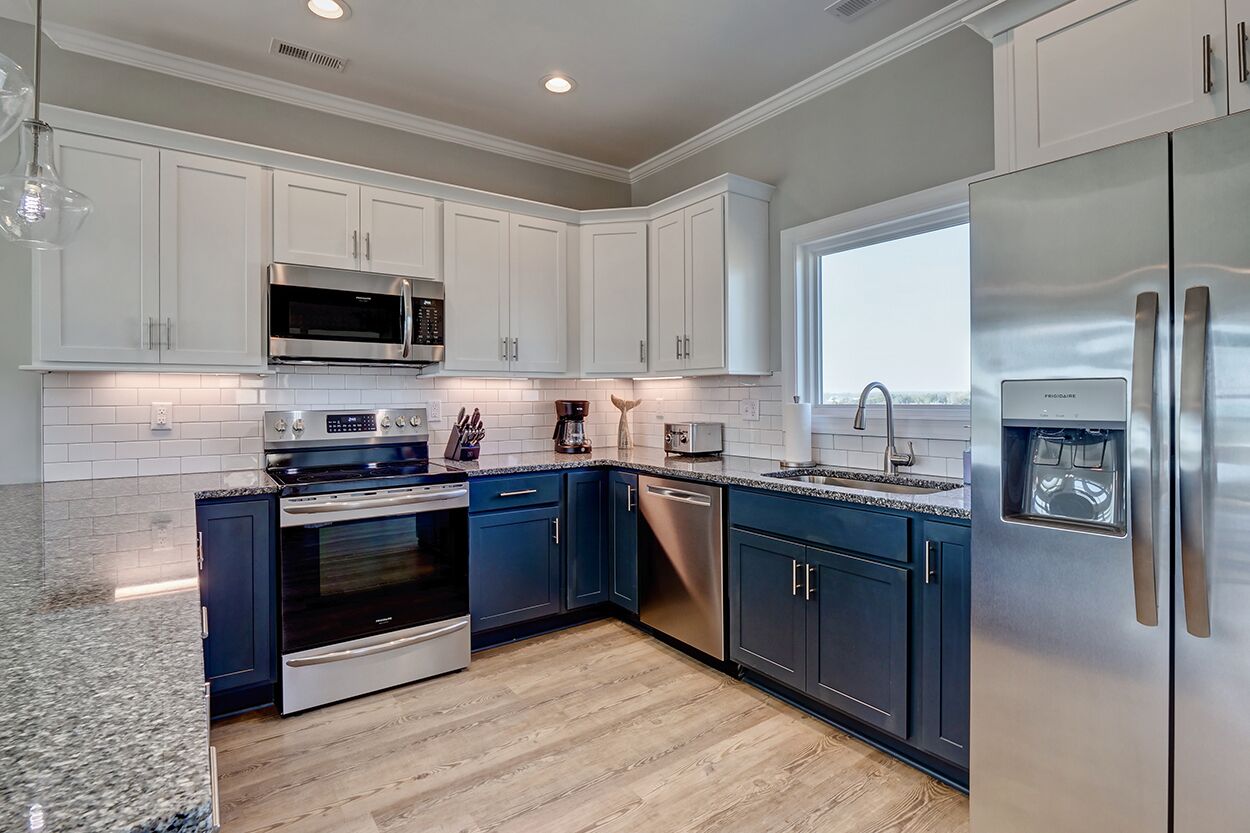 A modern kitchen with white cabinets, stainless steel appliances, and a large window providing natural light.