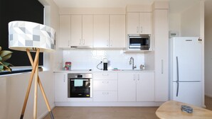 Eine moderne Küche mit weißen Schränken, einer Mikrowelle, einem Kühlschrank, einem Herd und einer Kaffeemaschine.
