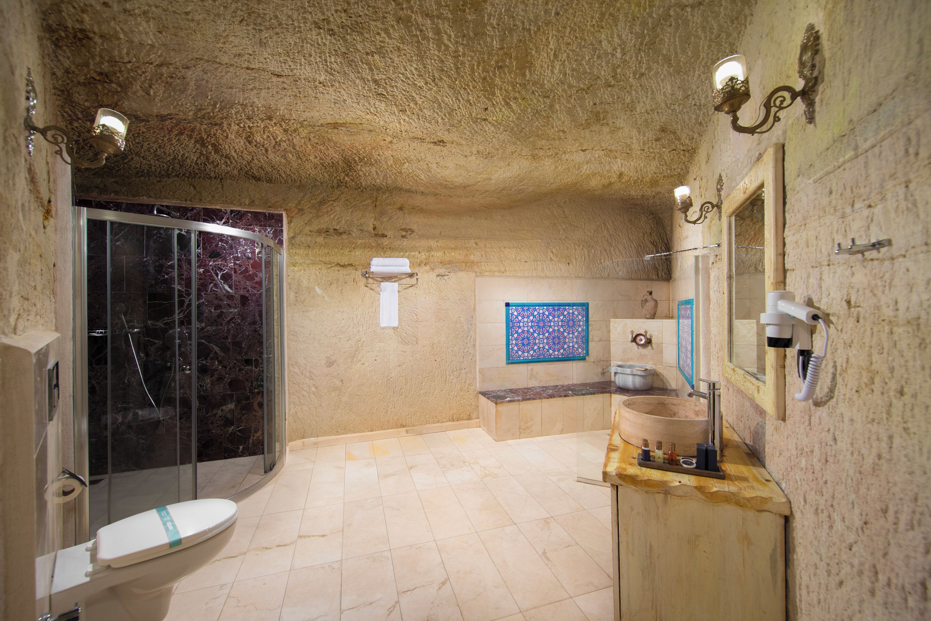 Un baño con ducha de mármol, inodoro, lavamanos con encimera de madera y espejo adosado a la pared.