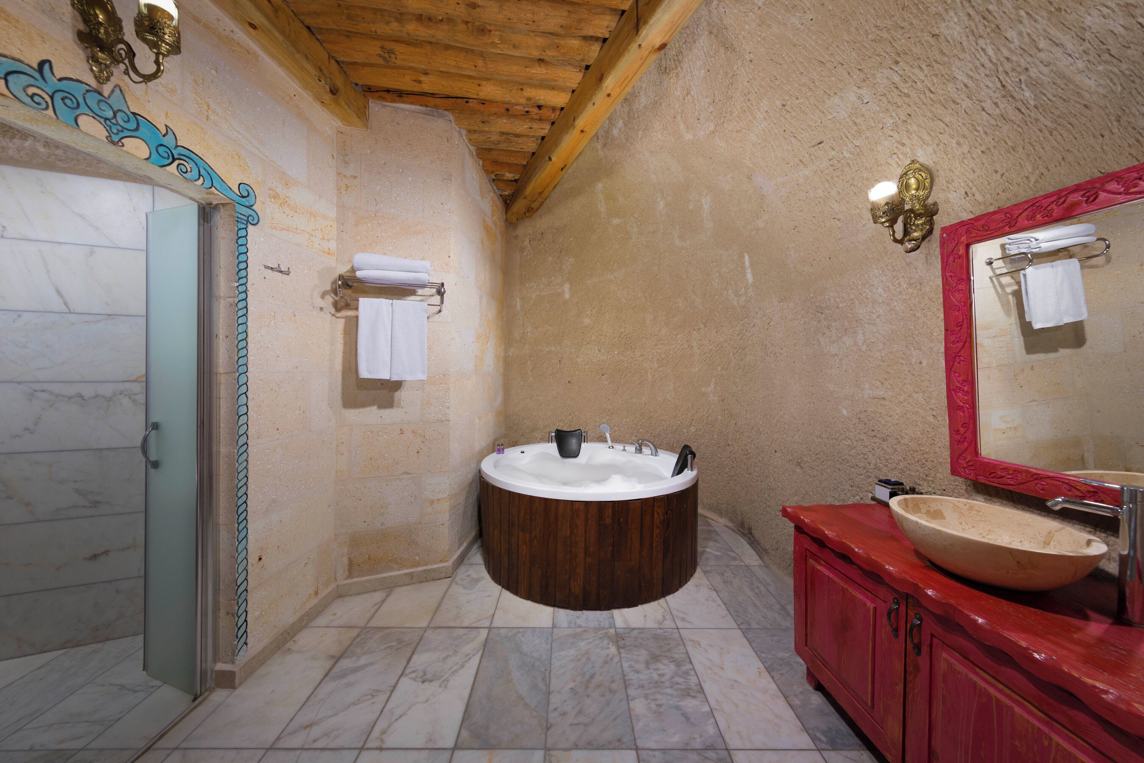 A bathroom with a wooden bathtub, a large mirror, and a red vanity.