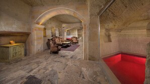 A stone-walled room with a red-tiled pool, wooden furniture, and a stone floor. - Turkan Cave Hotel (Ürgüp)