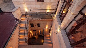 A multi-level stone building with a central staircase, multiple windows, and a metal railing. - Turkan Cave Hotel (Ürgüp)