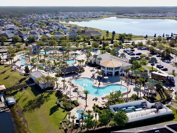 A resort with multiple swimming pools, a central pavilion, and a view of a lake.
