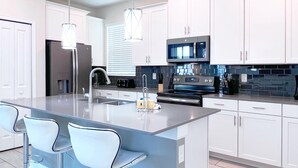 A modern kitchen with white cabinets, stainless steel appliances, and a central island with bar stools. - WATERPARK! Mickey & Superhero! EPIC Resort Close 2 Disney! 2730 (Kissimmee)