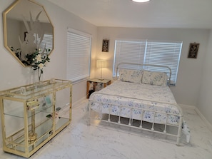 A bedroom with a bed, a bedside table, a mirror, and a window with blinds. - Complete Remodel Charmin home near bush garden,hard rock casino, Moffitt,Usf!! (Tampa)