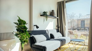 A modern living room with a sofa, a potted plant, a small table, and a view of the outside.