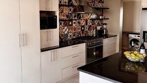 Cozinha moderna com armários brancos, bancada preta e azulejos de parede estampados.