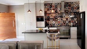 Cozinha moderna com ilha central, iluminação pendente e detalhes no revestimento da parede.
