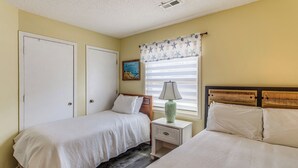 Un dormitorio con dos camas, una mesita de noche, una lámpara, un cuadro y una ventana con cortinas.