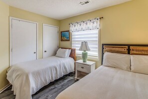 A bedroom with two beds, a nightstand, a lamp, a painting, and a window with curtains.