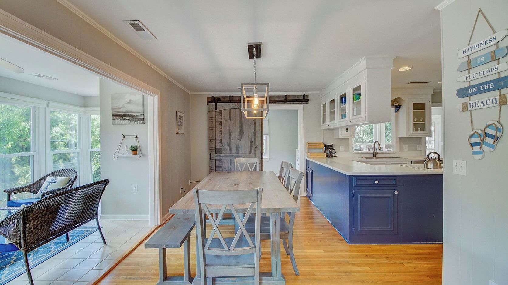 A modern kitchen with a central island, wooden flooring, and a dining area with wicker chairs.