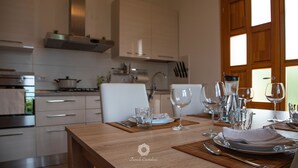 A modern kitchen with white cabinets, a wooden table set for dining, and a view of the outdoors through a window.