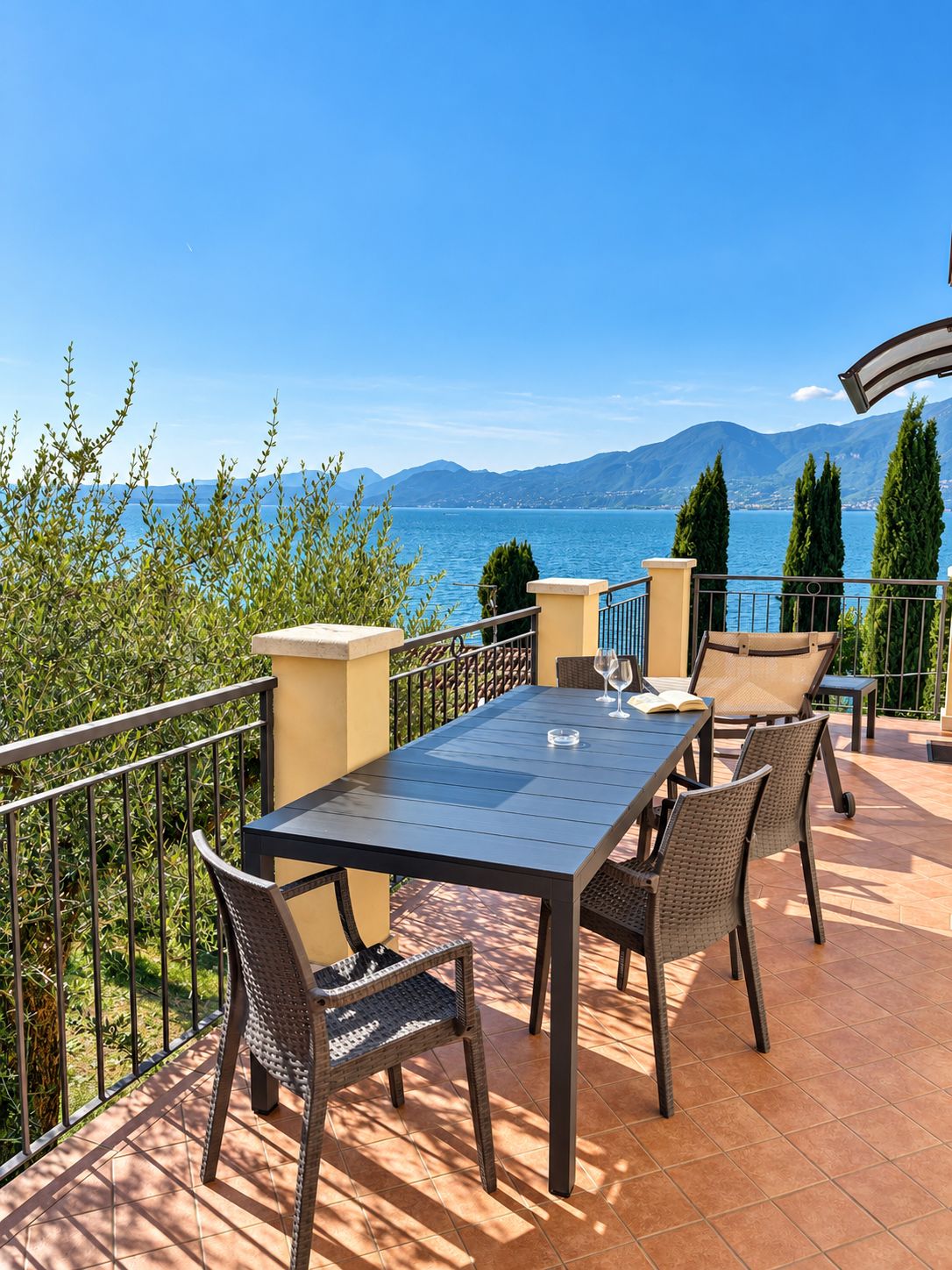 Une terrasse avec une table et des chaises, donnant sur un plan d’eau et des montagnes.