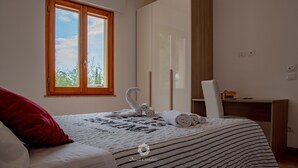 A bedroom with a bed, a window with a view, a wardrobe, and a desk.