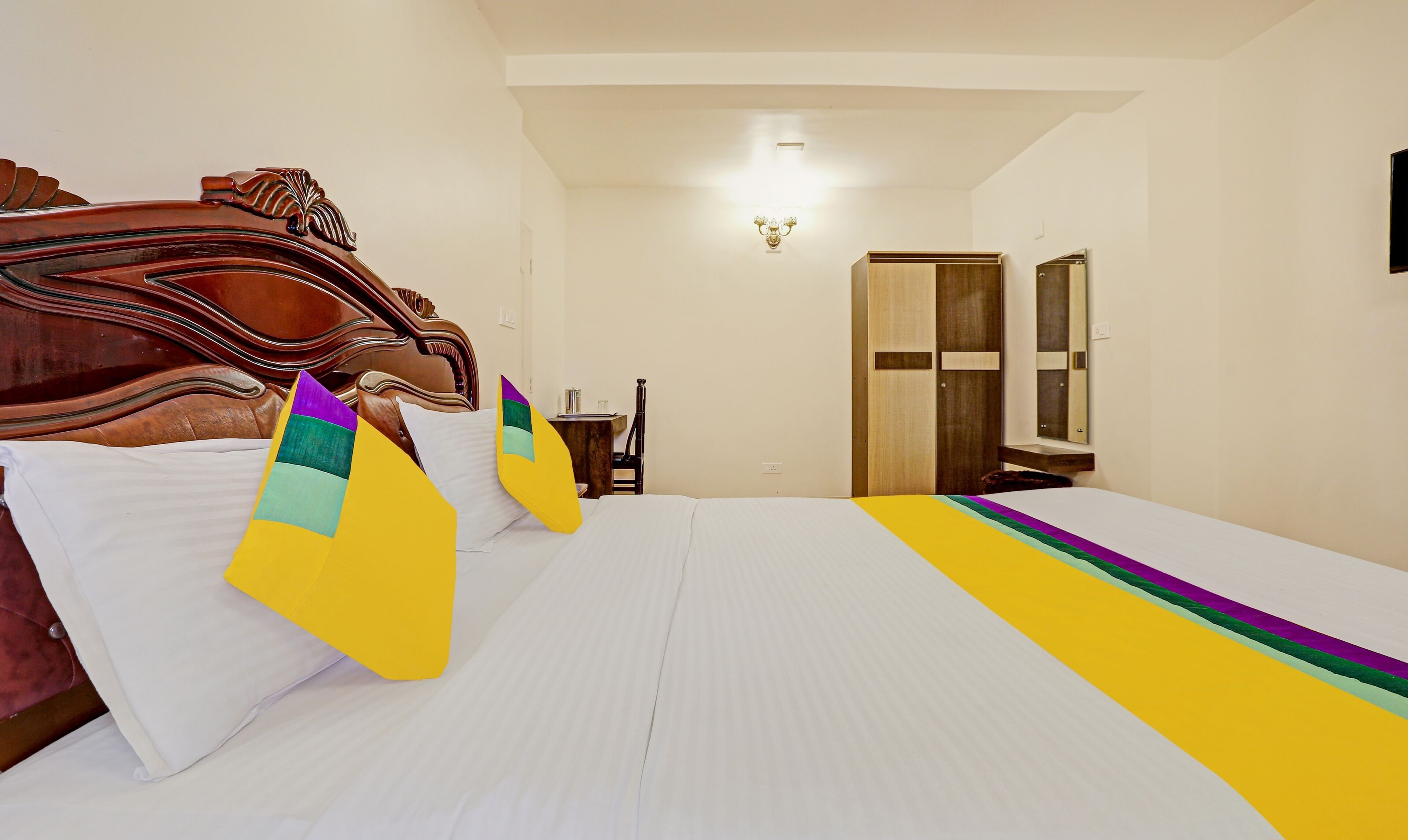 Ein Hotelzimmer mit einem großen Bett, einem Holzkopfende, einem Nachttisch, einem Spiegel und einem Kleiderschrank.