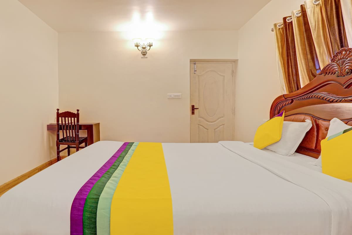 Un dormitorio con una cama, una silla de madera, una mesita de noche, un televisor montado en la pared y una puerta con cortinas.