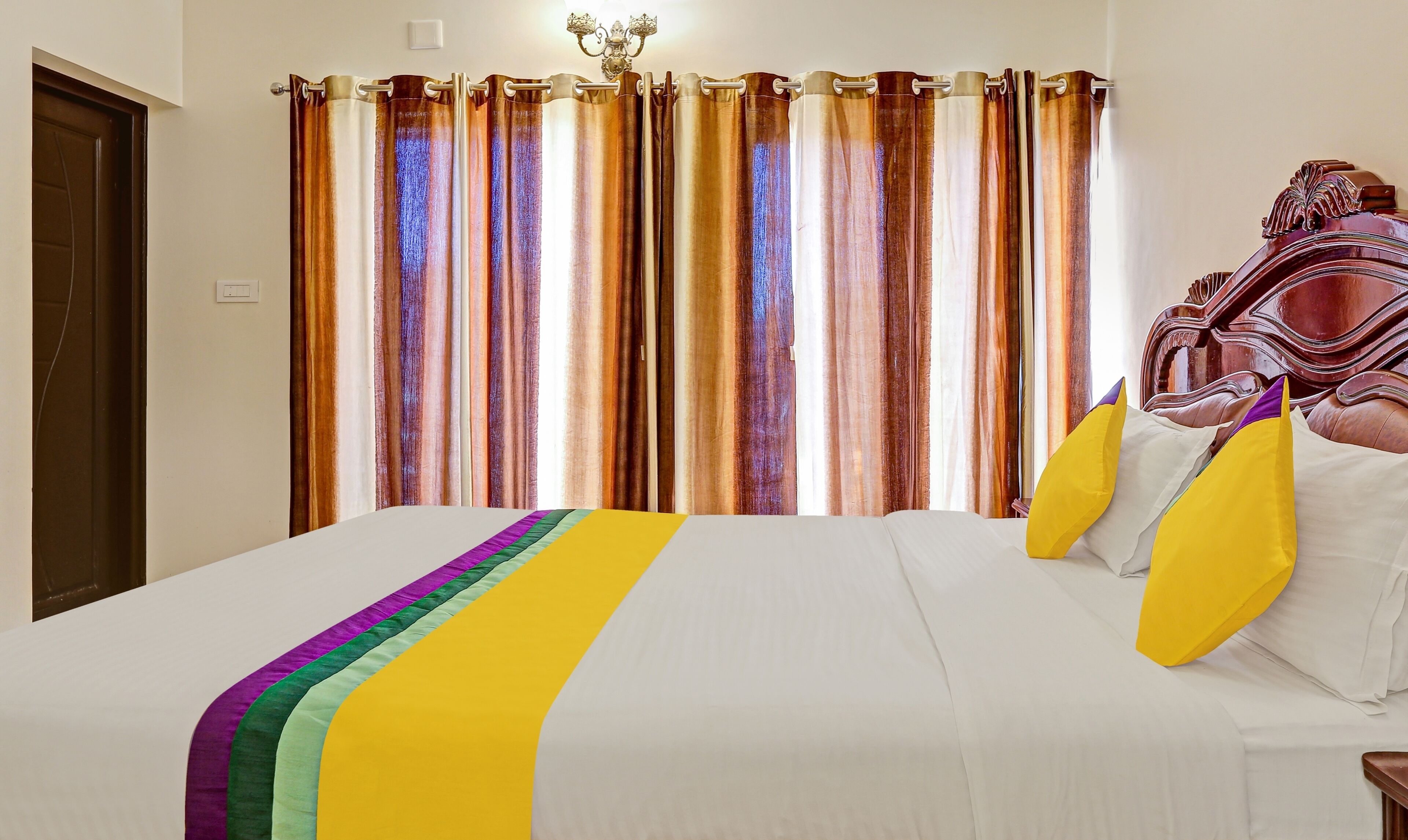 A hotel room with a large bed, a wooden headboard, and curtains with a gradient color pattern.
