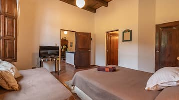 A hotel room with two beds, wooden ceiling beams, a television, and a small kitchenette.