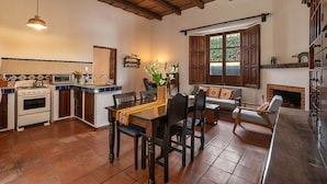 A spacious kitchen with a dining area, wooden beams, a fireplace, and a large window. - Casita del Escritor (Antigua Guatemala)