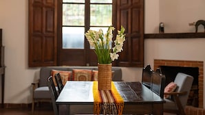 A dining table with a woven centerpiece, a striped table runner, and a fireplace in the background. - Casita del Escritor (Antigua Guatemala)